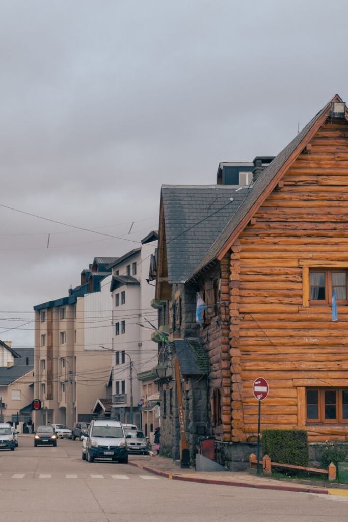 A charming log cabin stands at a street corner beside urban buildings under overcast skies.