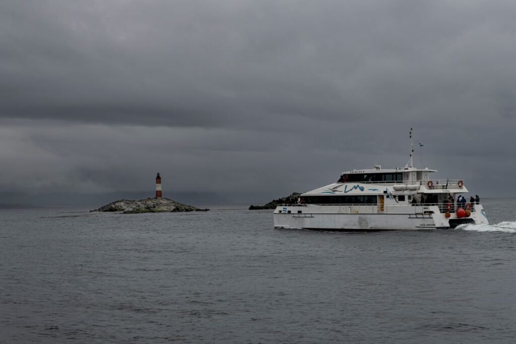 A catamaran sails near Les Eclaireurs Lighthouse under cloudy skies in Ushuaia, Argentina.